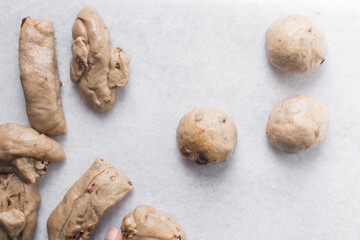 Overhead view of Hot cross bun dough being rolled into balls on a marble countertop, process of making hot cross buns