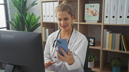 A young caucasian woman in a white lab coat smiling at her smartphone in a modern clinic office