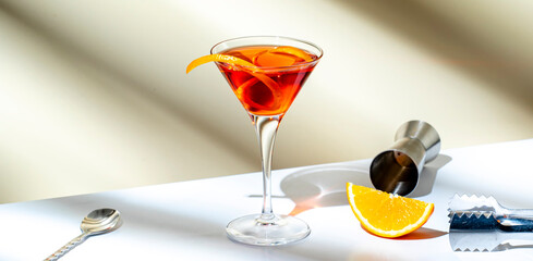 Orange cocktail with red vermouth, liqueur, bitter, citrus zest and ice in martini glass on beige...