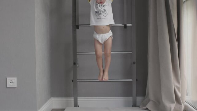 Boy hangs from pull-up bar on wall enjoying sports playful and energetic side of childhood. Child exercising on wall hanging from bar capturing joy and activity of sporty childhood