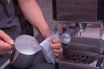 A woman barista operates a machine to prepare coffee, milk aeration process.