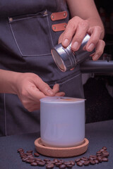 A woman barista operates a coffee brewing machine, pouring cinnamon into a cup of cappuccino coffee.