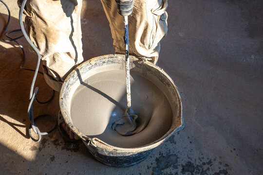 Mixing cement mortar during construction. Human uses equipment to prepare building materials. Using construction mixer. Repair work. Mixing liquid self-leveling floor in bucket. Cement fluid