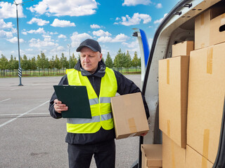 Positive delivery guy. Courier with clipboard stands on street. Postman delivered parcels by car. Courier in reflective vest. Delivery man loads boxes into minivan. Happy postman. Parcel logistics