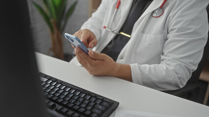 Hispanic doctor examines patient information on smartphone in hospital office, evoking healthcare technology.