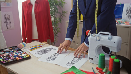 A well-dressed man examines fashion sketches in a colorful tailor shop with sewing machine and fabric.