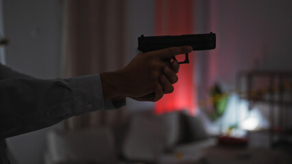 Close-up of a man's hand holding a pistol indoors with dim lighting and a hint of red illumination...