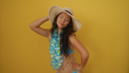 Beautiful young asian woman in bikini and summer hat posing against a vibrant yellow background