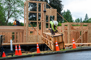 Residential house construction, boom crane truck delivering lumber to job site, wood support truss beams, worker connecting lift chain to beam  © knelson20