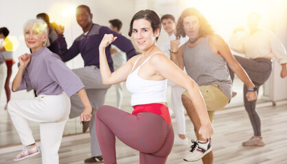 Obraz premium Smiling young woman rehearsing modern dance with group in dance school