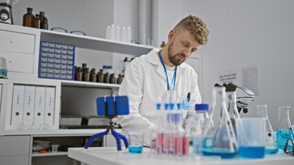 Naklejka premium A bearded caucasian man in a lab coat examines chemicals in a modern laboratory setting, representing research.