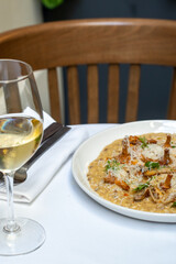 Creamy risotto with wild mushrooms and glass of white wine on elegant table setting. Concept of fine dining, gourmet cuisine, and culinary presentation. High quality photo