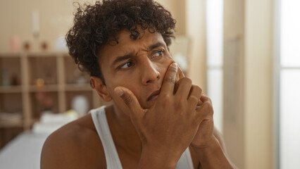 Young hispanic man in a spa thinking deeply while sitting indoors in a serene wellness center