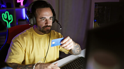 Handsome hispanic man with beard holding credit card in dark gaming room at night. © Krakenimages.com