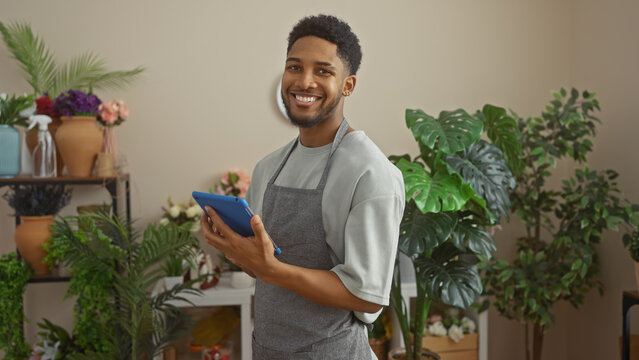 Smiling african american man with tablet in a flower shop surrounded by green plants