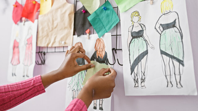 African american woman working in a design atelier with sketches and fabric swatches on display - Powered by Adobe