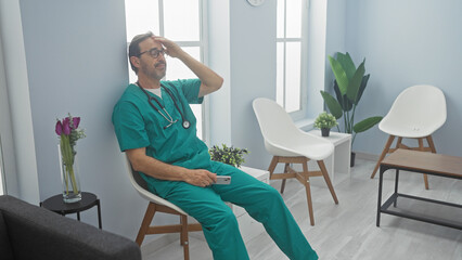 A middle-aged male doctor in scrubs looks exhausted in a modern hospital waiting room