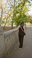 Fototapeta premium A young woman walks contemplatively in an autumnal park with balustrade and fallen leaves.
