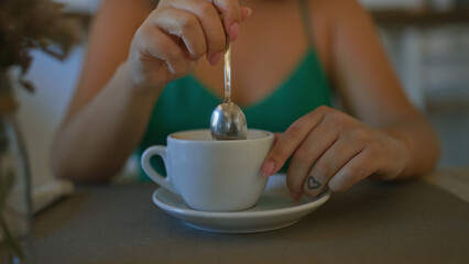 Young hispanic woman stirring coffee at a cafeteria in italy with a tattooed heart on her finger.