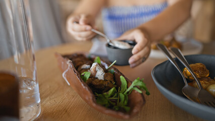 Young hispanic woman putting sauce on meat dish at the restaurant
