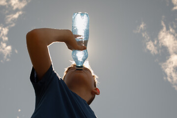 Child drinking water from bottle on a hot summer day, thirsty little boy drinks from water bottle...
