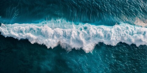 Aerial shot capturing a dramatic wave cresting in deep blue ocean with sharp contrast of white foam