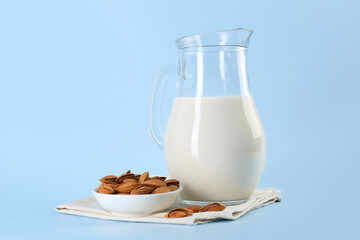 Fresh almond milk in glass jug and nuts on light blue background