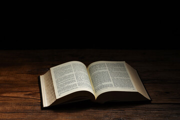 Obraz premium Bible on wooden table against black background, space for text. Religion of Christianity