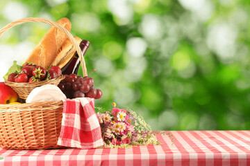 Picnic basket with foods and wine on table in nature. Space for text