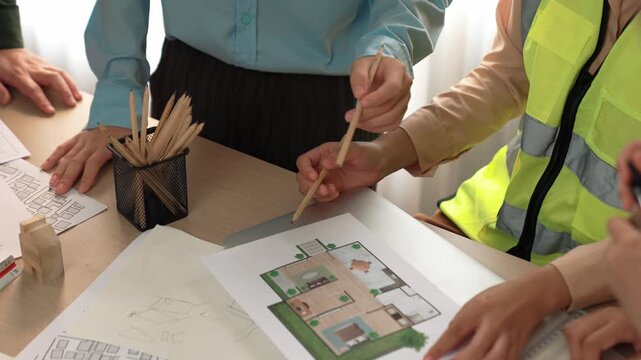 Smart architect and safety engineer discussion about building blueprint on table with architectural document, measurement tools and wooden block scatter around at modern office. Closeup. Delineation.