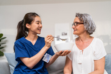 Asian caregiver nurse serve food to Caucasian senior older woman at home. 