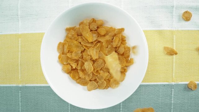 Close up of a healthy yellow cereal dropping in to bowl. Top down aerial view of cornflake falling into white bowl at white and black background. Macrography. Slow motion. Breakfast concept. Pabulum.