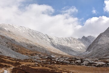 Panoramic shot of a wide clearing at the junction of two mountain ranges covered with the first snow on a cloudy autumn day.