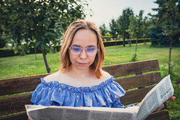 Young Woman Reading Newspaper While Relaxing on a Park Bench During a Sunny Afternoon