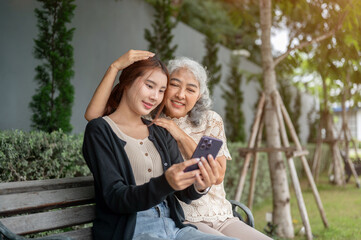 A lovely granddaughter and her grandma are sitting on a bench, watching a video on a phone together.