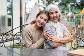 Naklejka premium A lovely Asian granddaughter and a happy grandma are sitting at a table outdoors together.