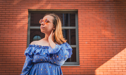 Young Woman in Blue Off-the-Shoulder Dress Posing Against Red Brick Wall on Sunny Day