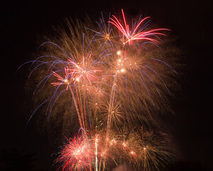 Multiple large fireworks exploding against a dark black night sky background with time lapse light trails and showers of sparks.