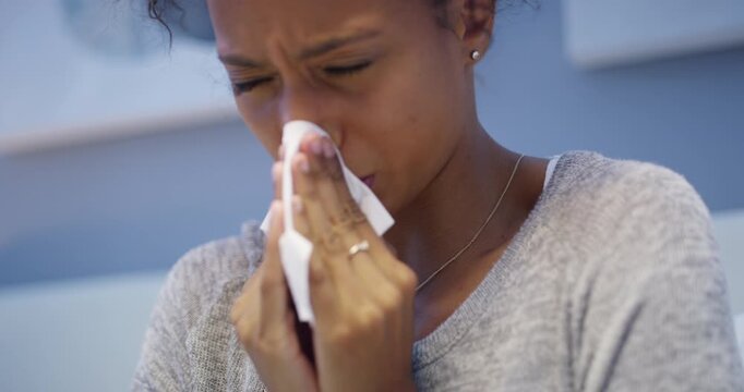 Cold, flu or sick woman sneezing, blowing her nose with tissue and suffering from a virus at home. Tired, ill and unhappy black female suffering from covid fatigue and resting in a bedroom alone