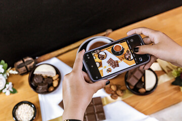 Woman with cell phone in her hand taking a picture of her chocolate business. International...