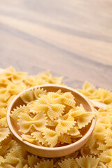 Uncooked farfalle pasta (bow tie shape) in wooden bowl, Italian food ingredient