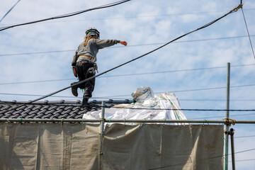 住宅の解体のために屋根の上で作業をする作業員