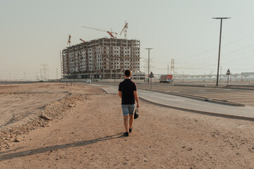 Man walking towards a construction site on a desert road carrying a bag