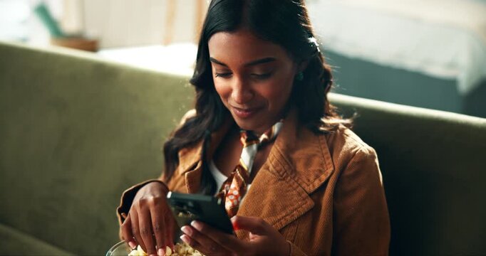 Popcorn, smartphone and woman relaxing on sofa watching funny video on social media or internet. Phone, smile and female person eating snack and reading comic blog on website in bedroom at apartment.