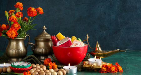 Diya lamps with candles, beads, marigold flowers and bowl of different treats on grunge green background. Divaly celebration