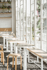 A minimalist coffee shop interior with white walls and wooden furniture. Large windows let in abundant natural light, creating a bright and airy atmosphere