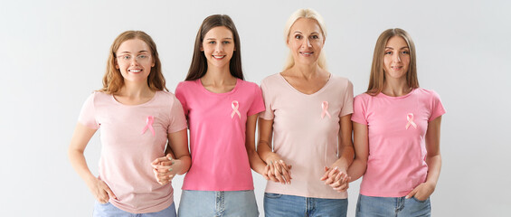 Beautiful women with pink awareness ribbons holding hands on light background. Breast cancer concept