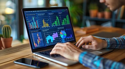 Man Working at a Wooden Desk, Focused on Laptop Displaying Colorful Charts and Graphs, Suggesting Data Analysis or Business Performance Metrics