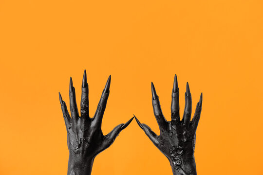 Black hands of witch on orange background. Halloween celebration