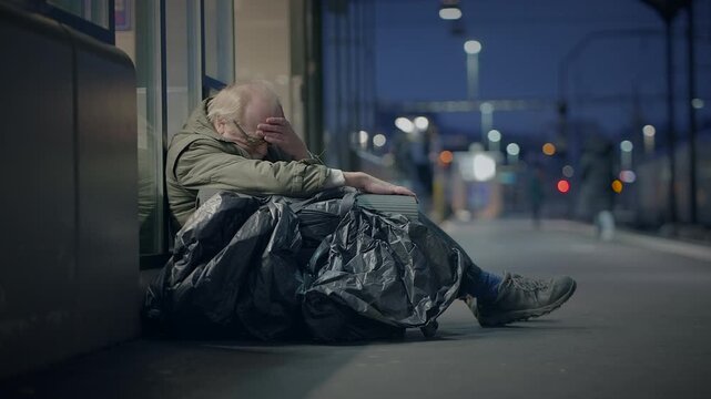 A person who is homeless sits on a city street at night, facing despair and loneliness